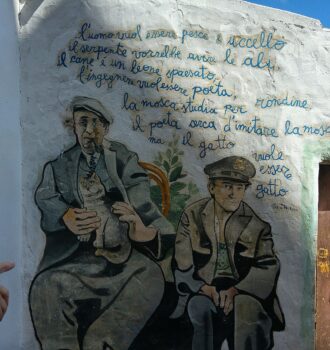 Murale di Orgosolo con due uomini e versi dipinti su un muro bianco