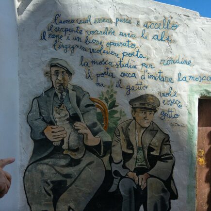 Murale di Orgosolo con due uomini e versi dipinti su un muro bianco